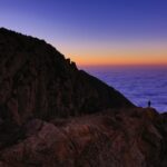 person standing on mountain in front of body of water