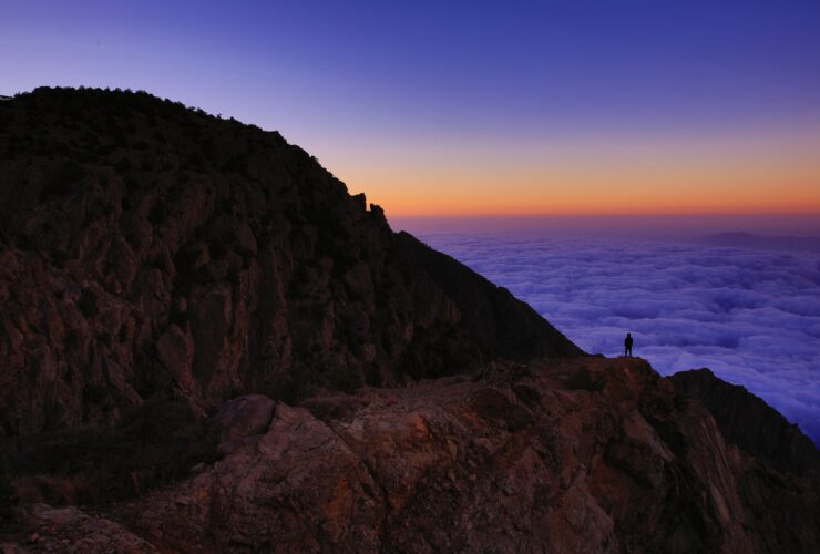 person standing on mountain in front of body of water
