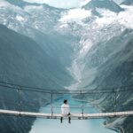 man wearing white shirt siting on bridge overlooking at mountain
