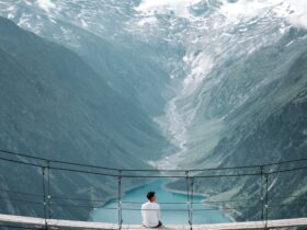 man wearing white shirt siting on bridge overlooking at mountain