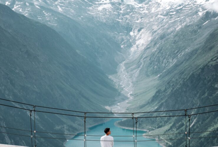 man wearing white shirt siting on bridge overlooking at mountain