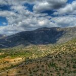 green grass field and mountains under white clouds and blue sky during daytime