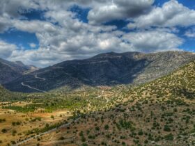 green grass field and mountains under white clouds and blue sky during daytime