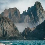 brown rocky mountain beside blue sea under white sky during daytime