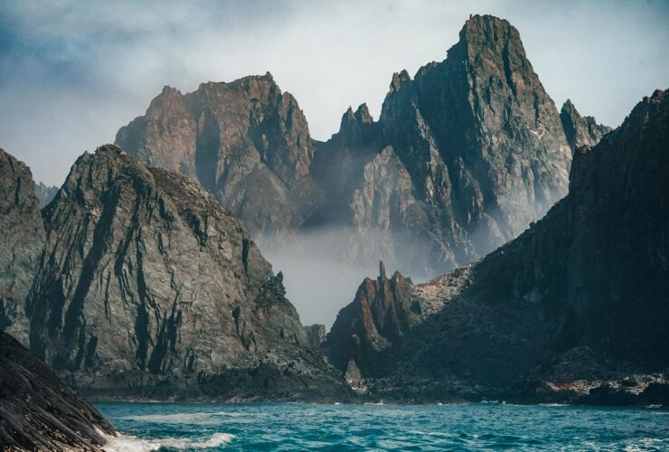 brown rocky mountain beside blue sea under white sky during daytime