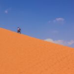 man in black shirt and blue denim jeans walking on brown sand during daytime