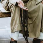 person in brown coat holding black beaded necklace