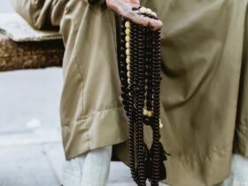 person in brown coat holding black beaded necklace