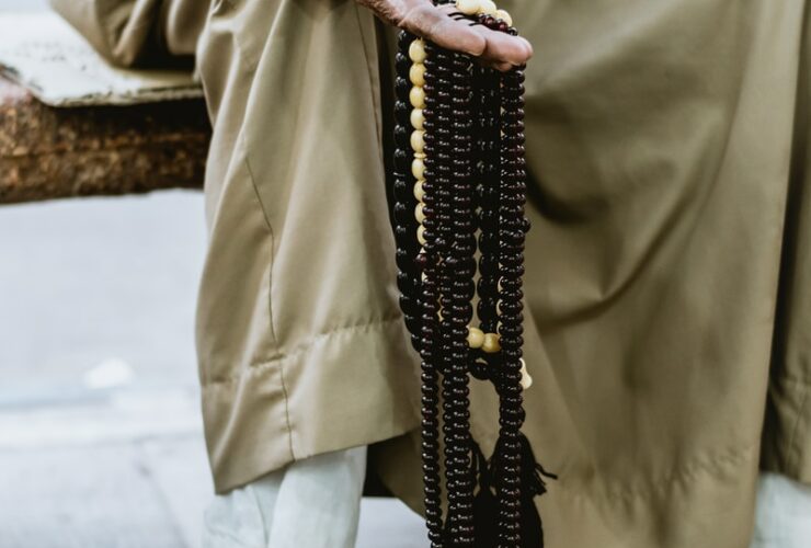 person in brown coat holding black beaded necklace