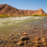 brown mountain beside body of water during daytime