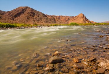 brown mountain beside body of water during daytime