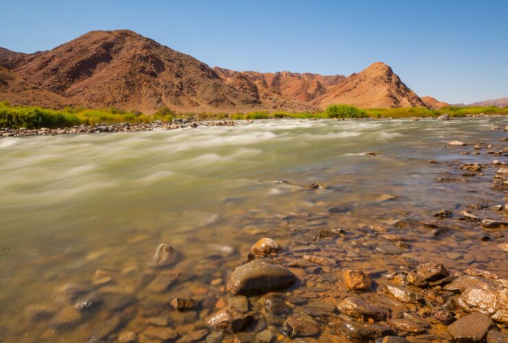 brown mountain beside body of water during daytime