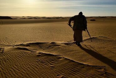 man in black shirt and black pants standing on brown sand during daytime