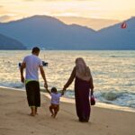 man and woman holding hands while walking on beach during daytime