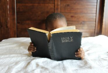 boy reading Holy Bible while lying on bed