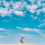 man and woman walking on brown sand under blue sky and white clouds during daytime