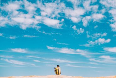 man and woman walking on brown sand under blue sky and white clouds during daytime