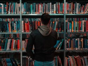 person wearing black and gray jacket in front of bookshelf