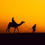 a person riding a camel in the desert at sunset