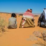 a couple of people sitting on top of a sandy field