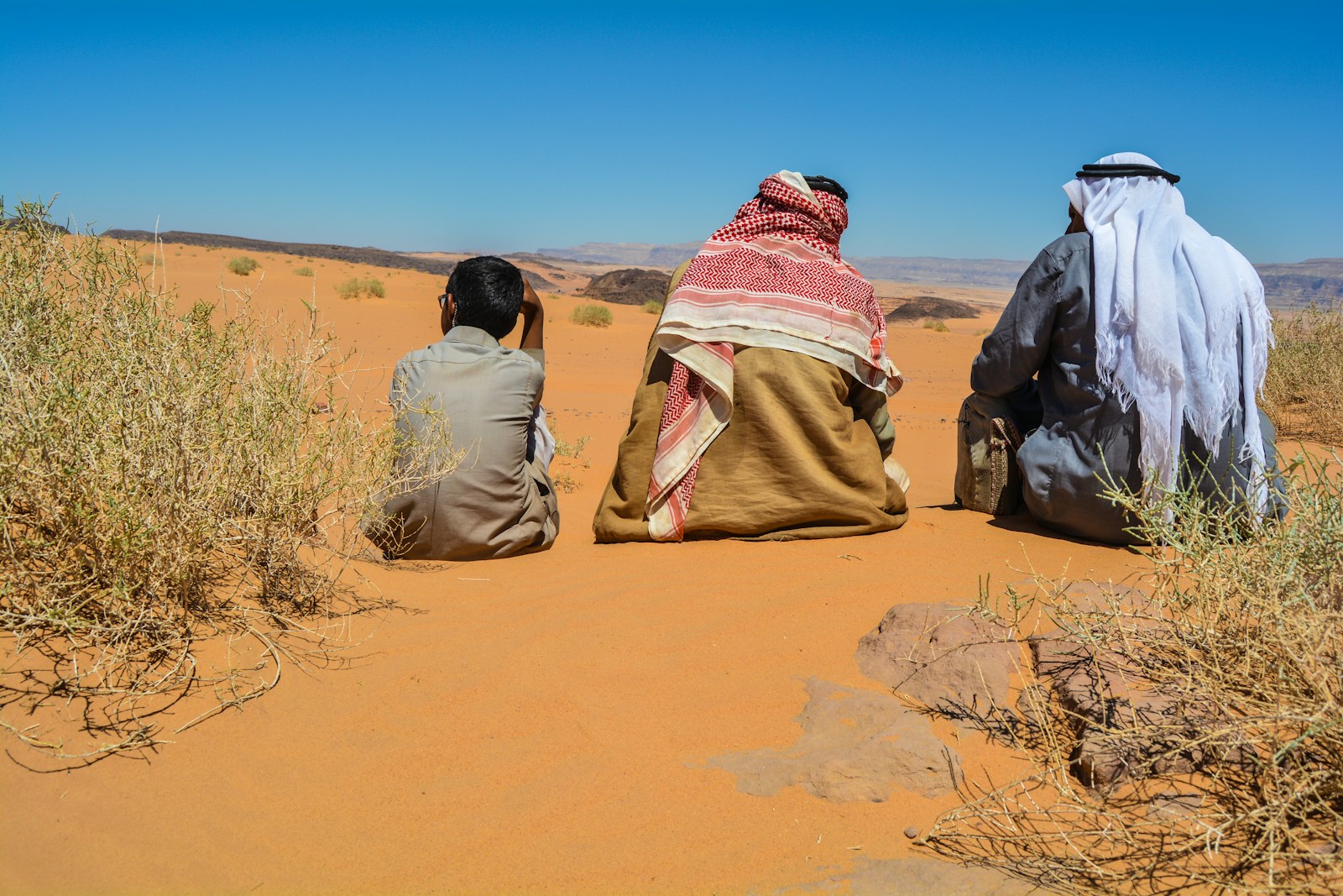 a couple of people sitting on top of a sandy field