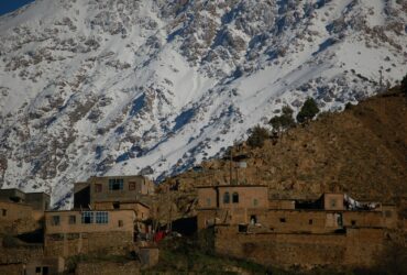 brown concrete building near snow covered mountain during daytime