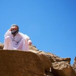 a man in a white robe and head covering standing on a rock