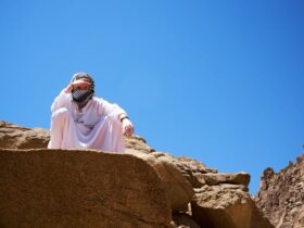 a man in a white robe and head covering standing on a rock