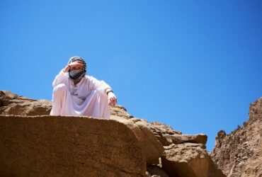 a man in a white robe and head covering standing on a rock