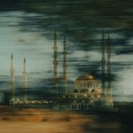 a building with a domed roof and towers with a body of water in the background